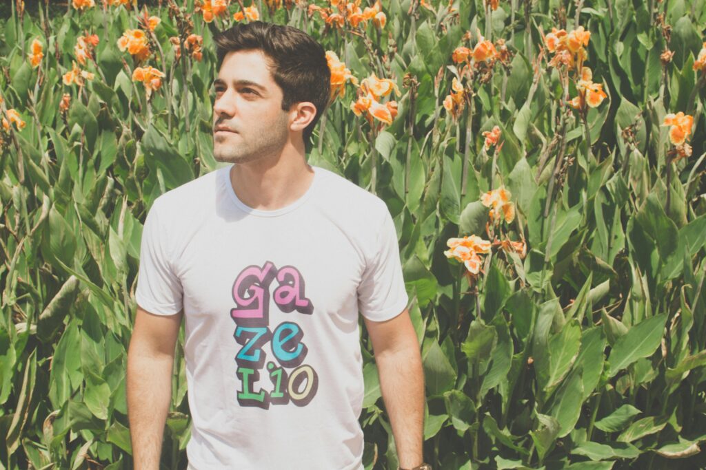 A young man poses confidently amidst colorful flowers and lush greenery in summer.
